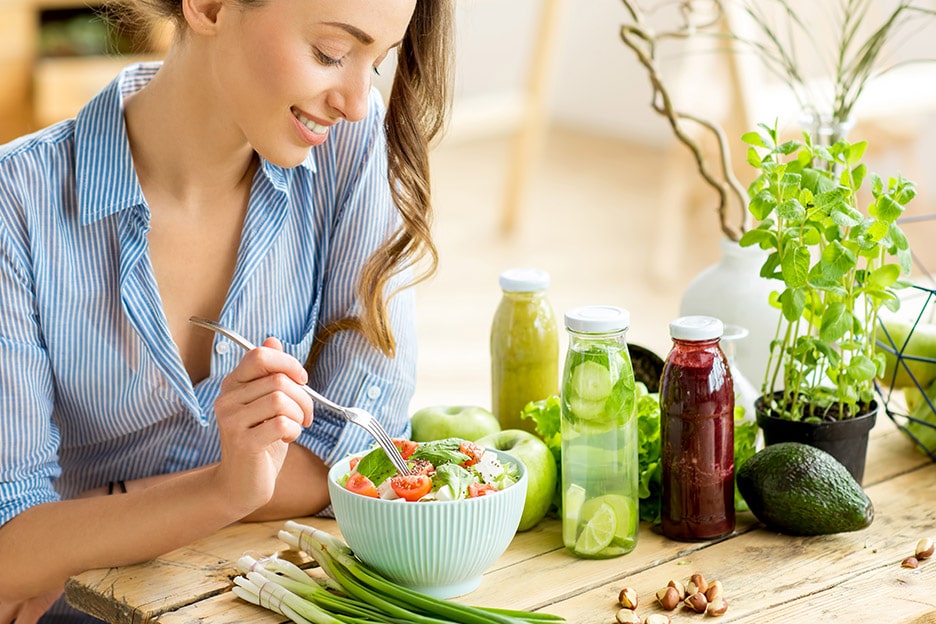 Lady sitting at a wooden table smiling eating salad - the mind-body connection